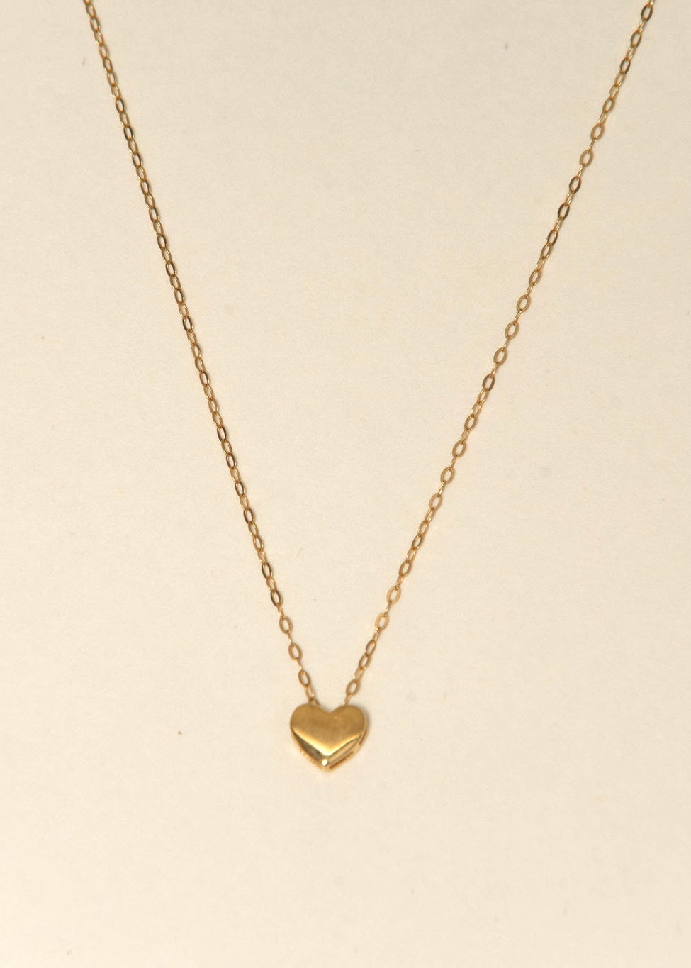 Gold heart-shaped pendant necklace on a beige background