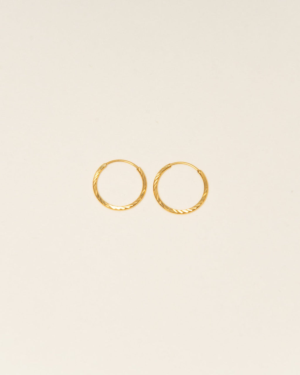 Two gold hoop earrings on a beige background