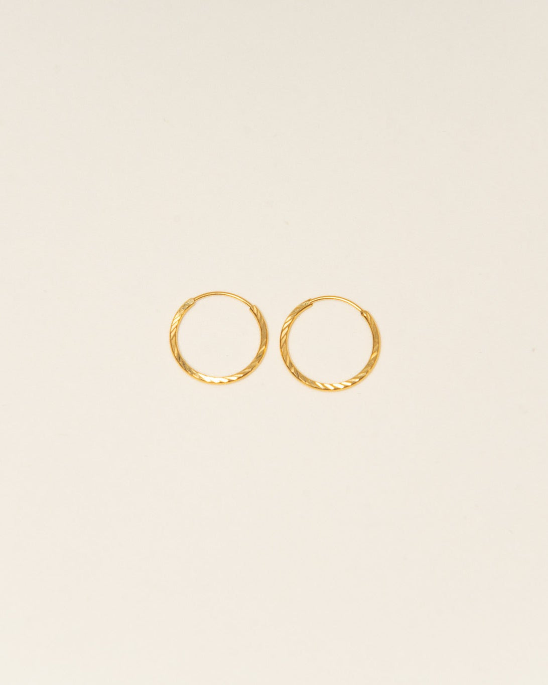 Two gold hoop earrings on a beige background