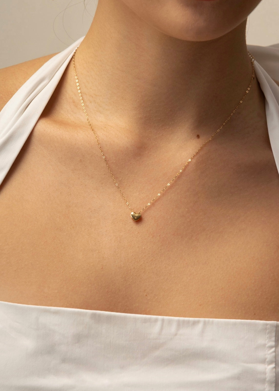 Gold heart necklace on a person wearing a white top against a neutral background