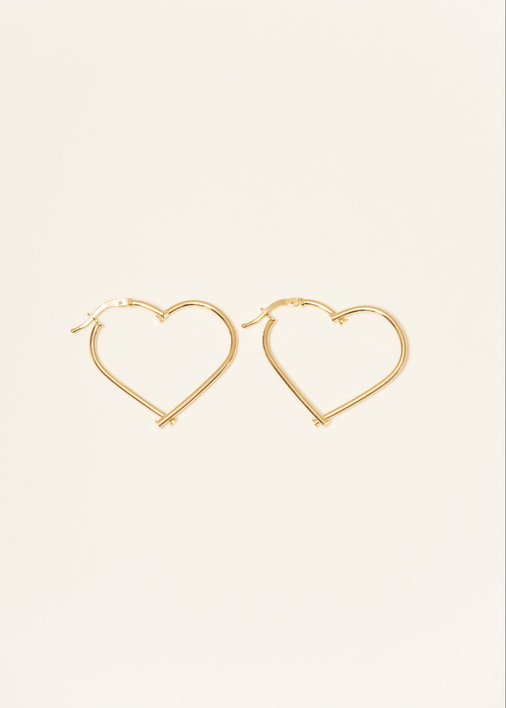 Gold heart-shaped hoop earrings on a light beige background