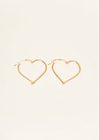 Gold heart-shaped hoop earrings on a light beige background