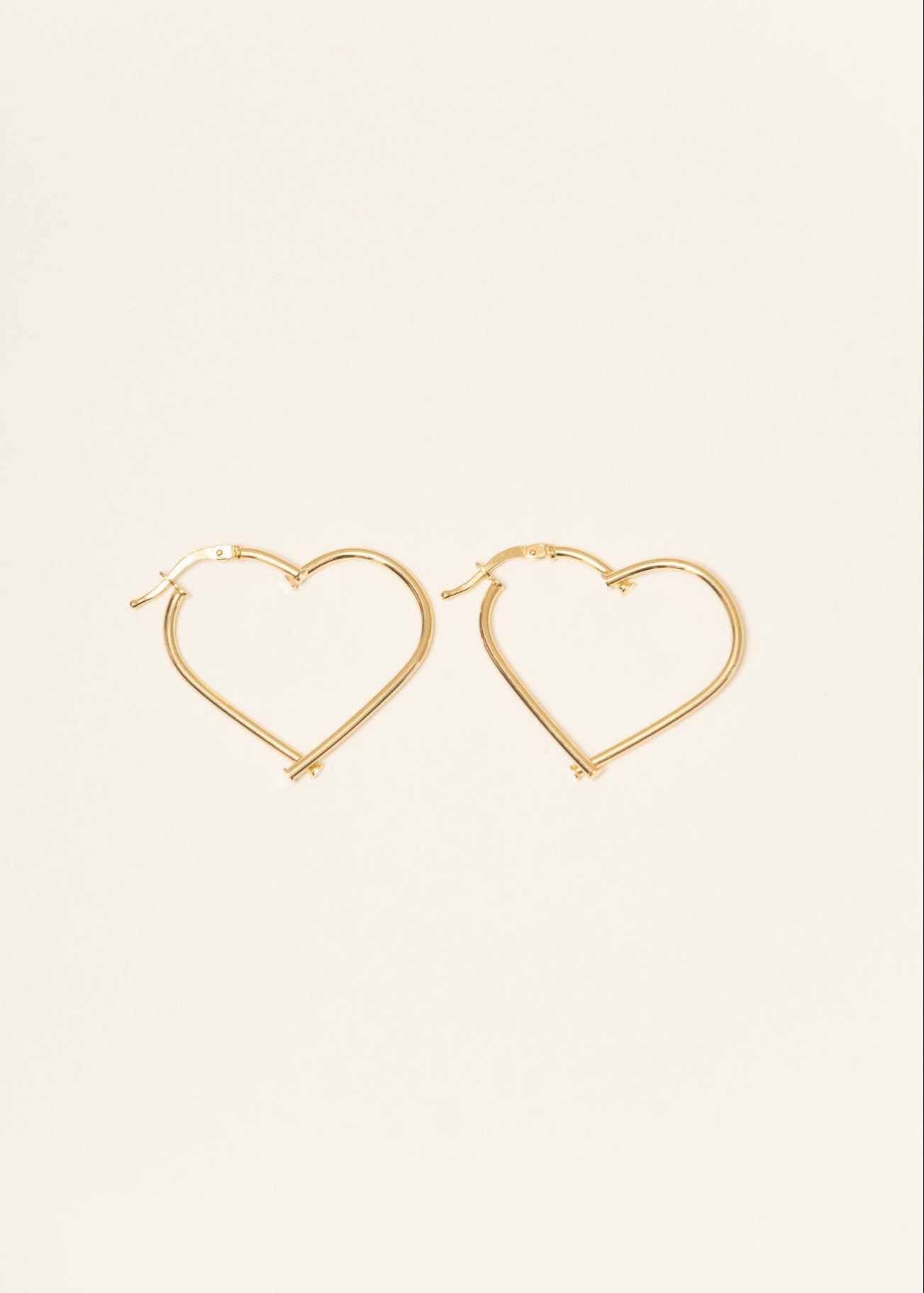 Gold heart-shaped hoop earrings on a light beige background